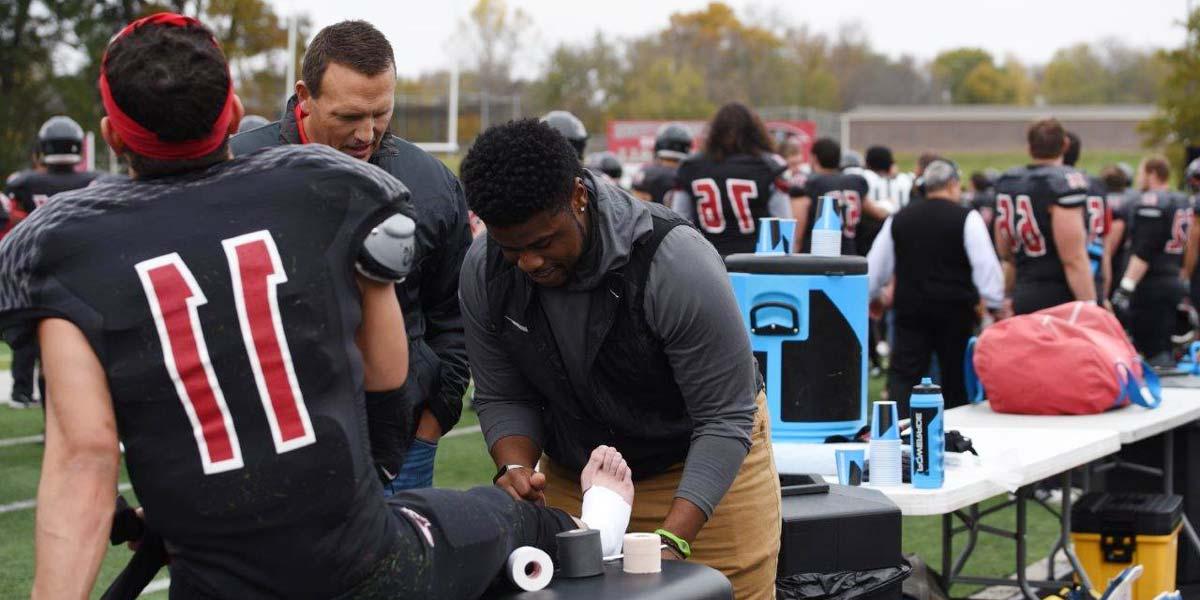 A student wraps a football student athlete's leg at a game