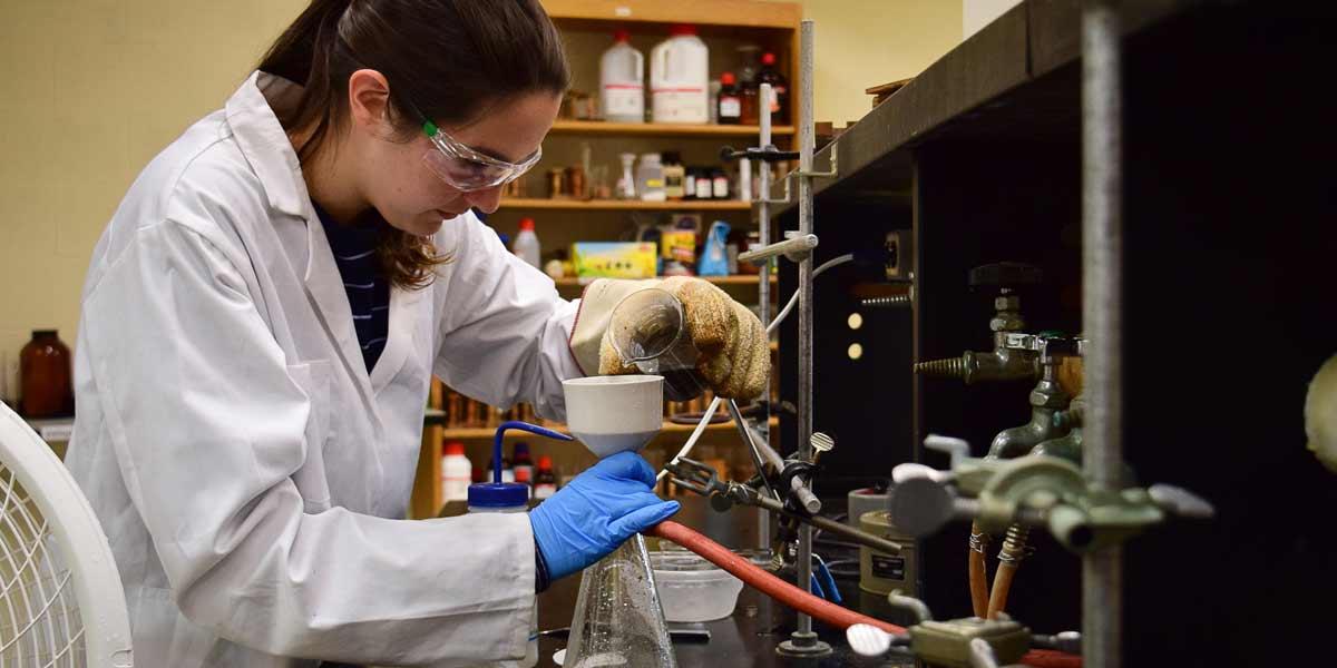 A female student pours from a beaker into a flask in Chemistry class