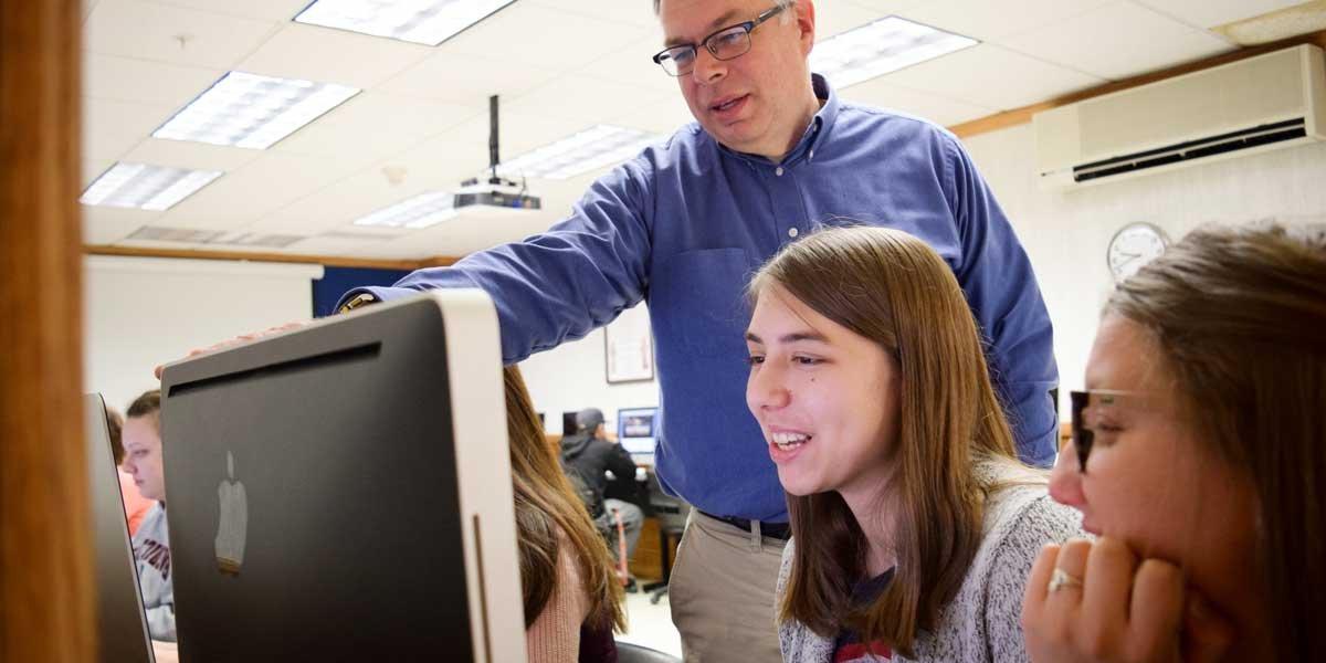 Professor Kevin Page works with students at a computer workstation